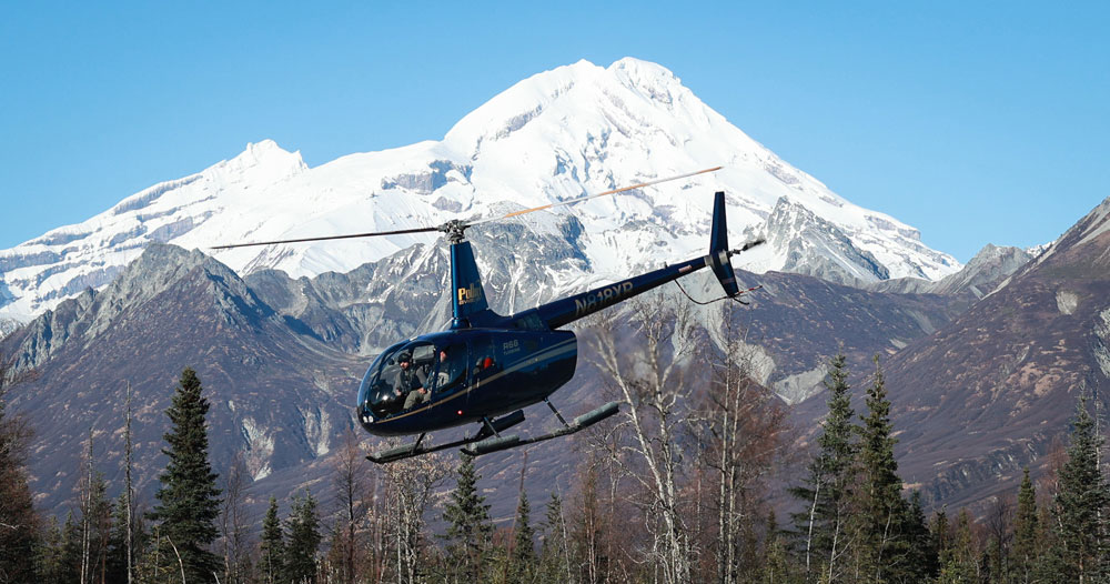 Helicopter flying away over the Kenai Peninsula river after dropping anglers at a remote fishing spot